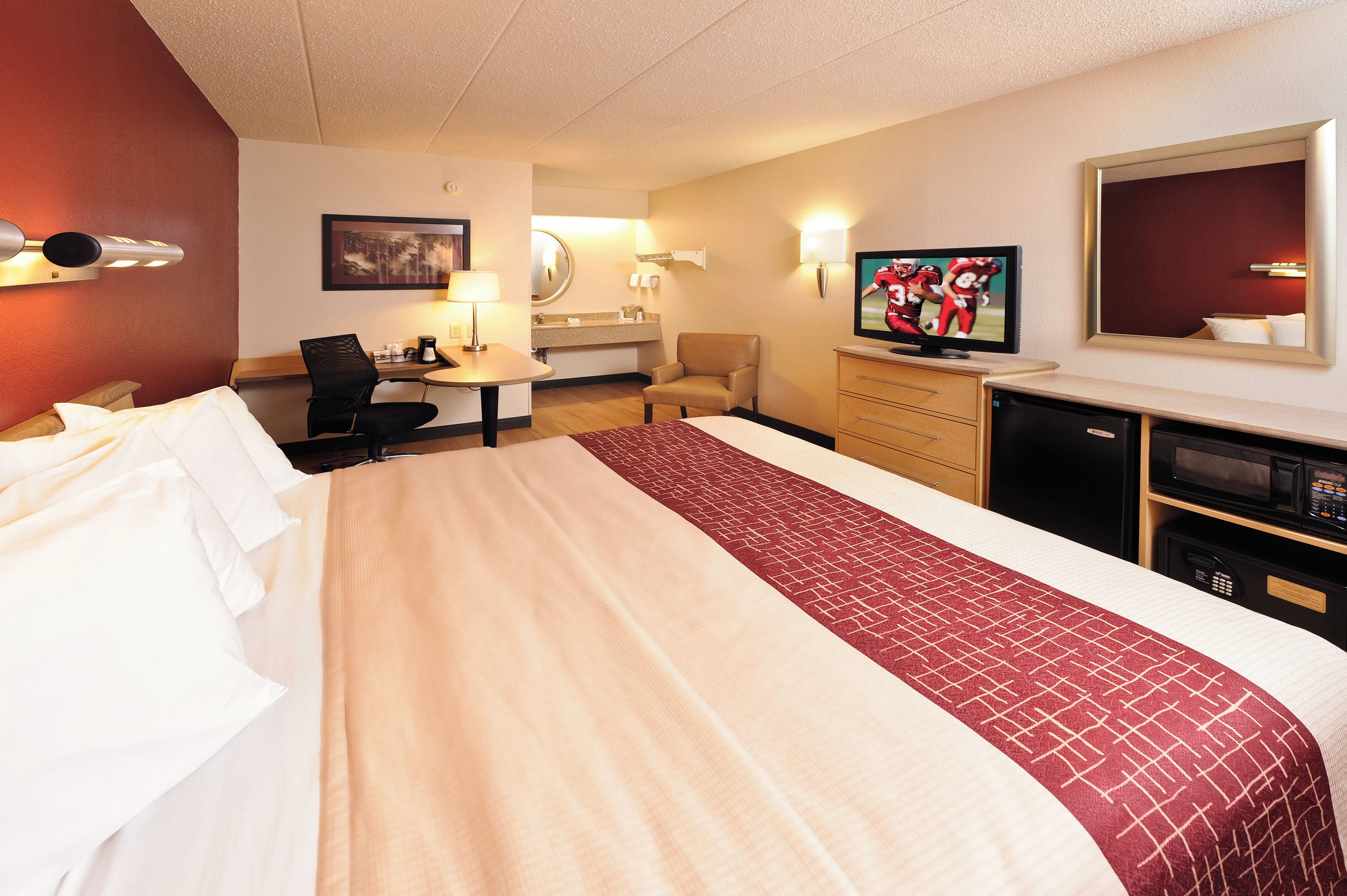 A hotel room with a large bed, a desk with a chair, a television, a mirror, and a minibar.