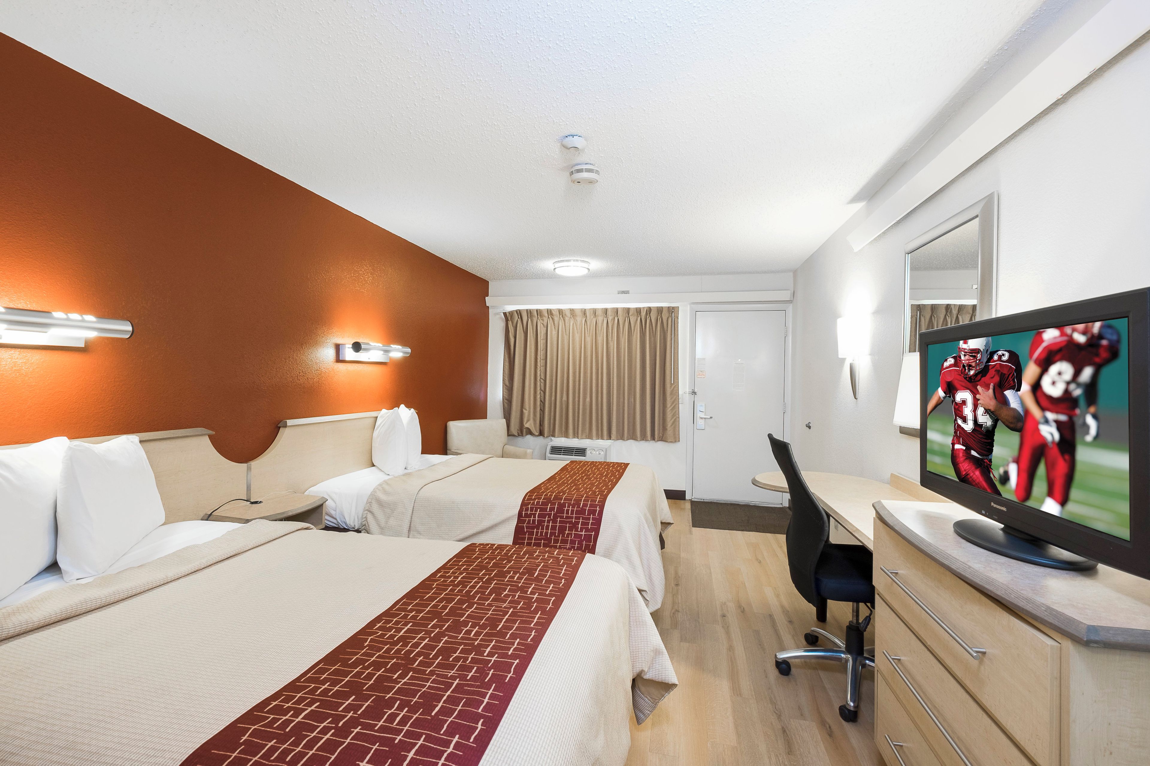 Una habitación de hotel con dos camas, un escritorio, un televisor y un espejo.