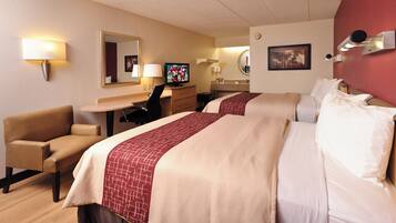 A hotel room with two beds, a desk, a chair, a television, and a bathroom.