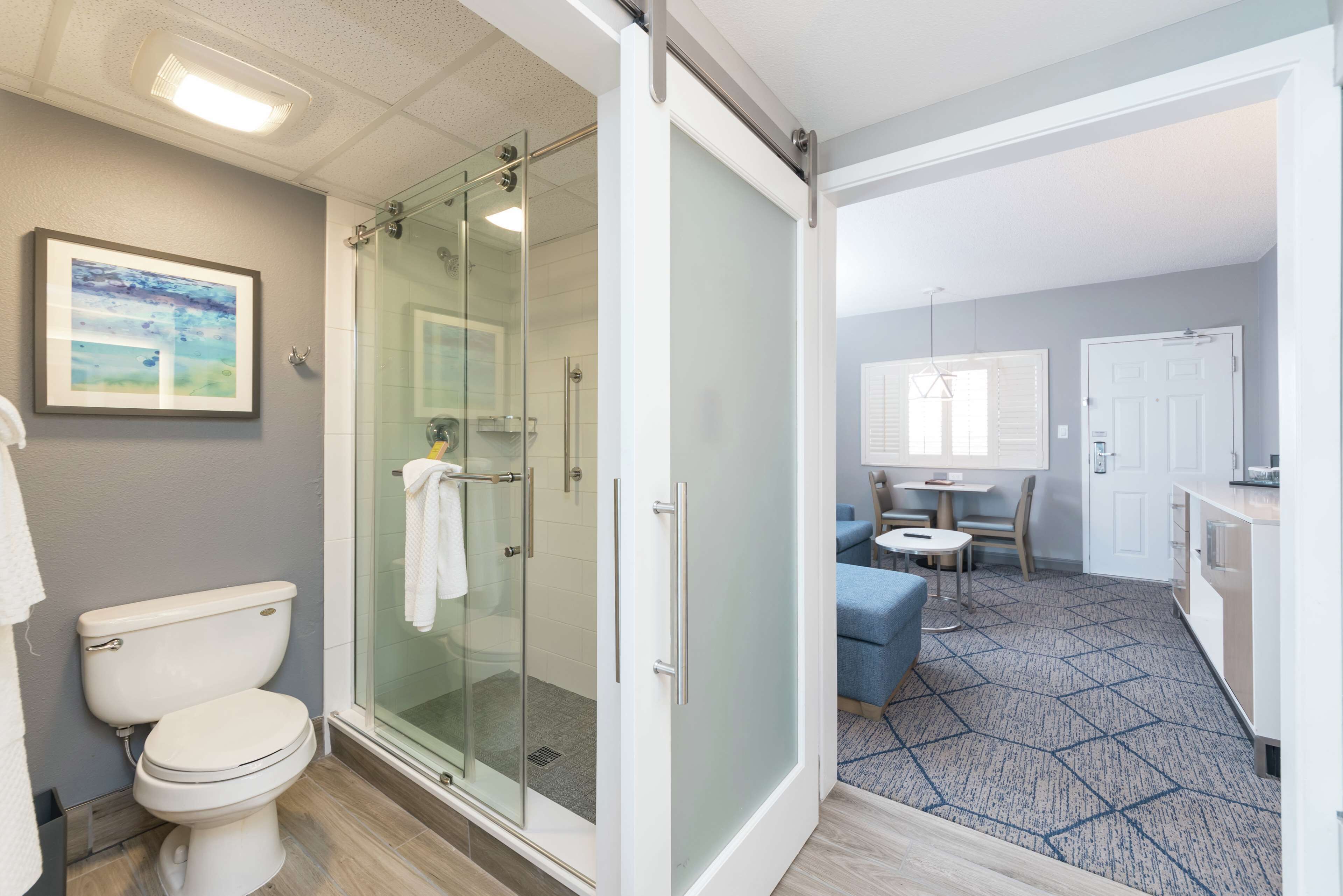 Un baño moderno con ducha de vidrio, inodoro y una pequeña zona de estar con mesa y sillas.