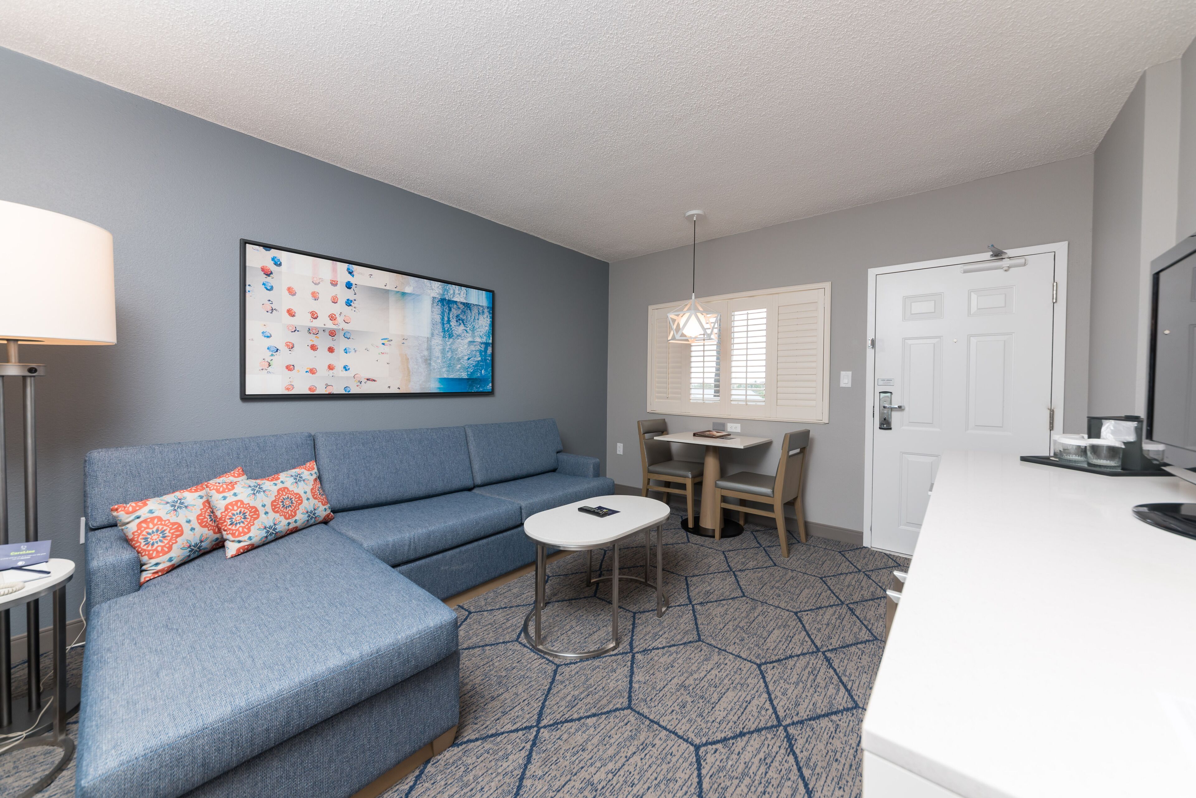 A modern living room with a blue sectional sofa, a small round table, and a kitchen area with a white countertop.