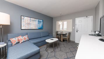 A modern living room with a blue sectional sofa, a small round table, and a kitchen area with a white countertop.