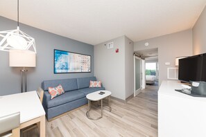 Ein modernes Wohnzimmer mit einem grauen Sofa, einem kleinen weißen Tisch, einer Stehlampe und einem Fernseher.