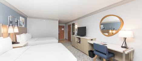 Habitación de hotel con dos camas, un escritorio, una silla, un televisor, un espejo y una lámpara.