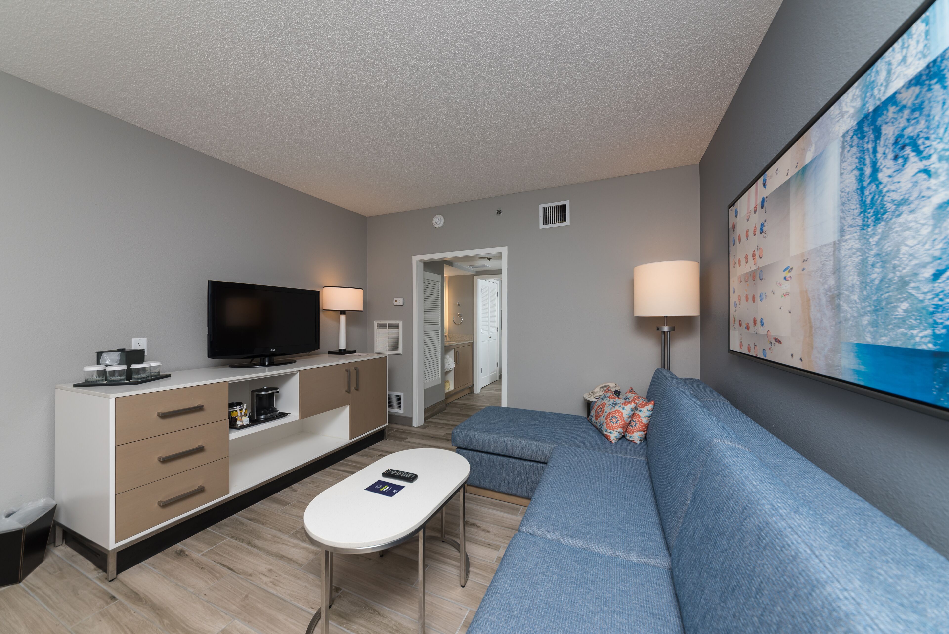 A modern living room with a flat-screen TV, a sofa, a coffee table, and a dining area with a cabinet and a lamp.