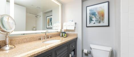 A modern bathroom with a granite countertop, a large mirror, a toilet, and a framed abstract painting on the wall.