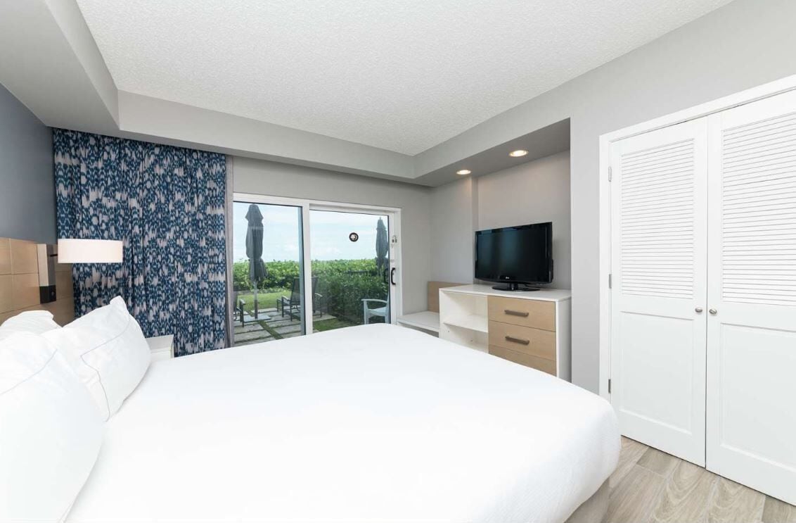 Een moderne hotelkamer met een groot bed, een televisie, een bureau en een schuifdeur naar een balkon.