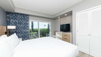 A modern hotel room with a large bed, a television, a desk, and a sliding glass door leading to a balcony.