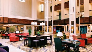 Eine großzügige Lobby mit hohen Decken, verschiedenen Sitzbereichen und einer zentralen Rezeption.