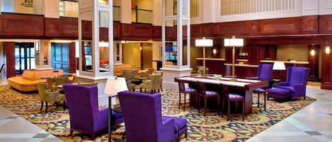 A spacious lobby with a checkered floor, purple armchairs, a wooden reception desk, and a large window.