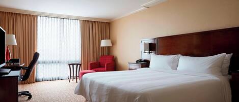 A hotel room with a large bed, a desk, a chair, a TV, and a window with curtains.