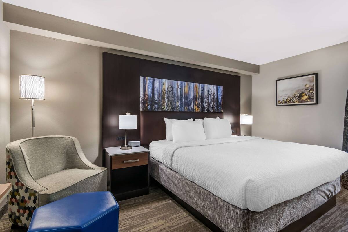 Ein Hotelzimmer mit Bett, Sessel, Schreibtisch und Nachttisch.