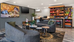 A modern lobby with grey sofas, a coffee table, a TV mounted on the wall, a desk with a computer, and a snack vending machine. - Best Western Atlanta-Marietta Ballpark Hotel (Marietta)