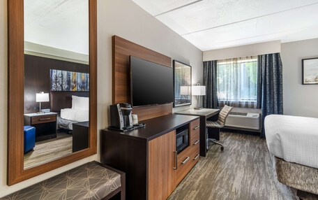 A hotel room with a large bed, a desk with a flat-screen TV, a coffee maker, a microwave, and a large mirror.