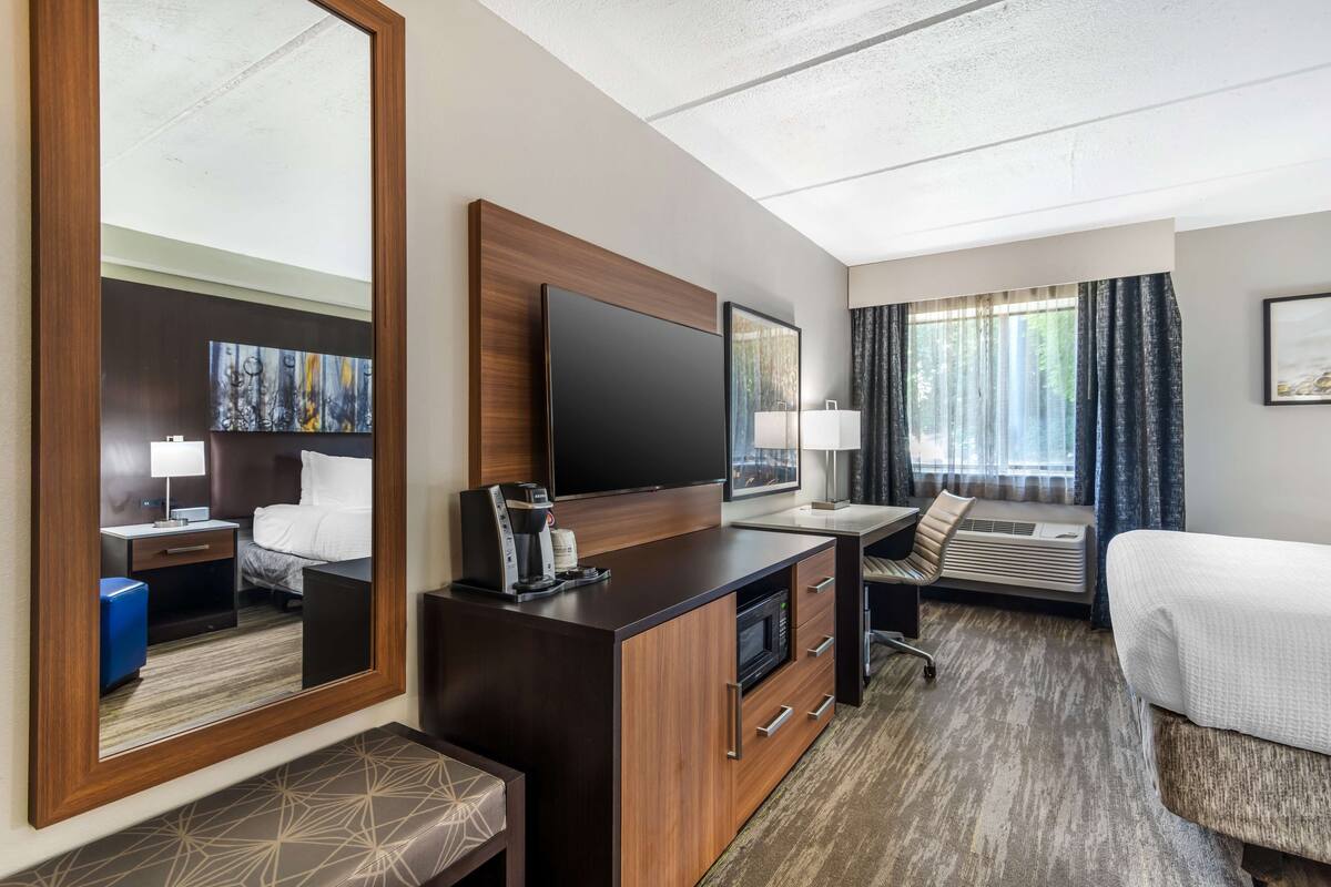 Ein Hotelzimmer mit einem großen Bett, einem Schreibtisch, einem Flachbildfernseher, einer Kaffeemaschine, einer Mikrowelle und einem großen Spiegel.