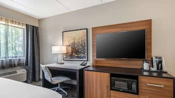 A hotel room with a bed, a desk with a lamp, a flat-screen TV, a coffee maker, and a microwave.