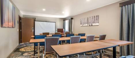 Une salle de conférence dotée d’un sol recouvert de moquette, de tables, de chaises et d’un écran de projection.