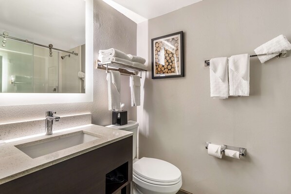 Un baño con cabina de ducha de vidrio, lavabo con grifo, inodoro y toallero con toallas.