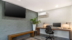 A modern office space with a large flat-screen TV, a wooden desk, a computer, a chair, a bench, and a potted plant. - Best Western Atlanta-Marietta Ballpark Hotel (Marietta)