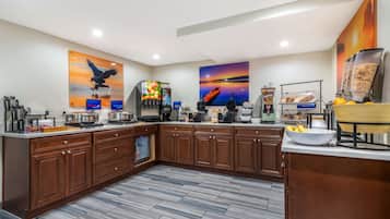 A modern kitchen with wooden cabinets, a large island, and a breakfast bar. There are two large paintings on the walls, a coffee machine, and a waffle maker.