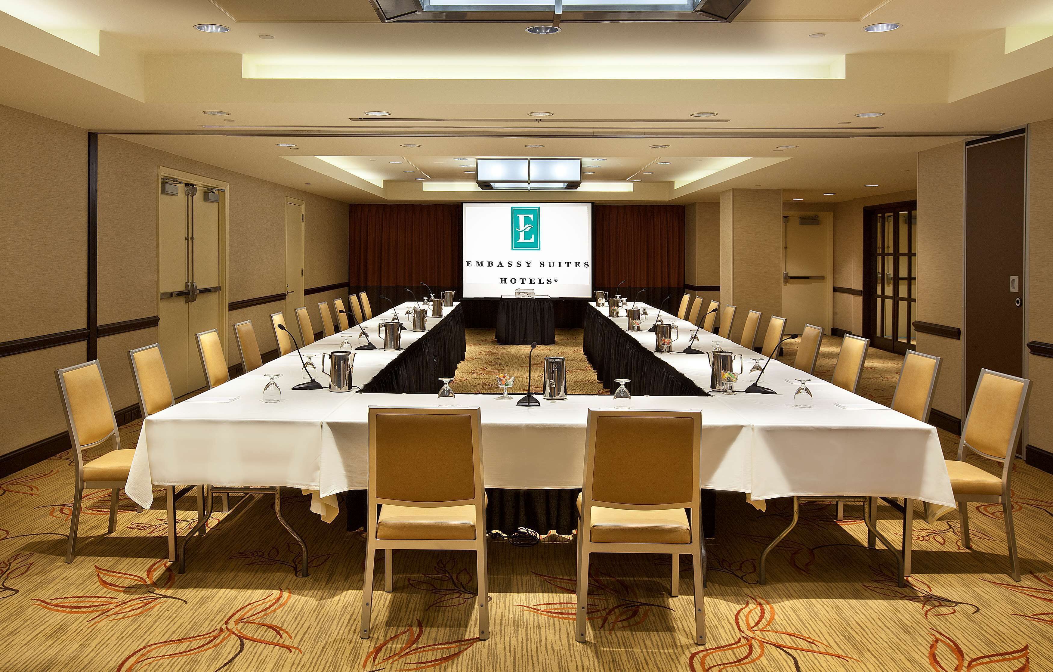 A conference room with a long table, chairs, and a projection screen displaying the logo of Embassy Suites Hotels.