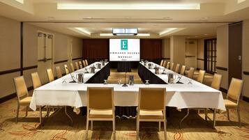 A conference room with a long table, chairs, and a projection screen displaying the logo of Embassy Suites Hotels.
