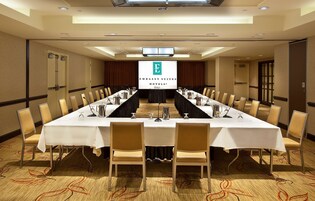 A conference room with a long table, chairs, and a projection screen displaying the logo of Embassy Suites Hotels.