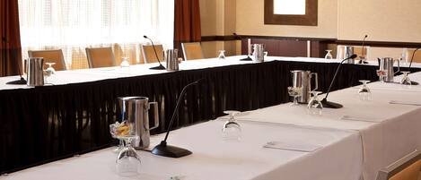 A conference room with a long table set for a meeting, equipped with microphones, glasses, and a pitcher.