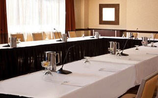Une salle de conférence avec une longue table préparée pour une réunion, équipée de microphones, de verres et d’une carafe.