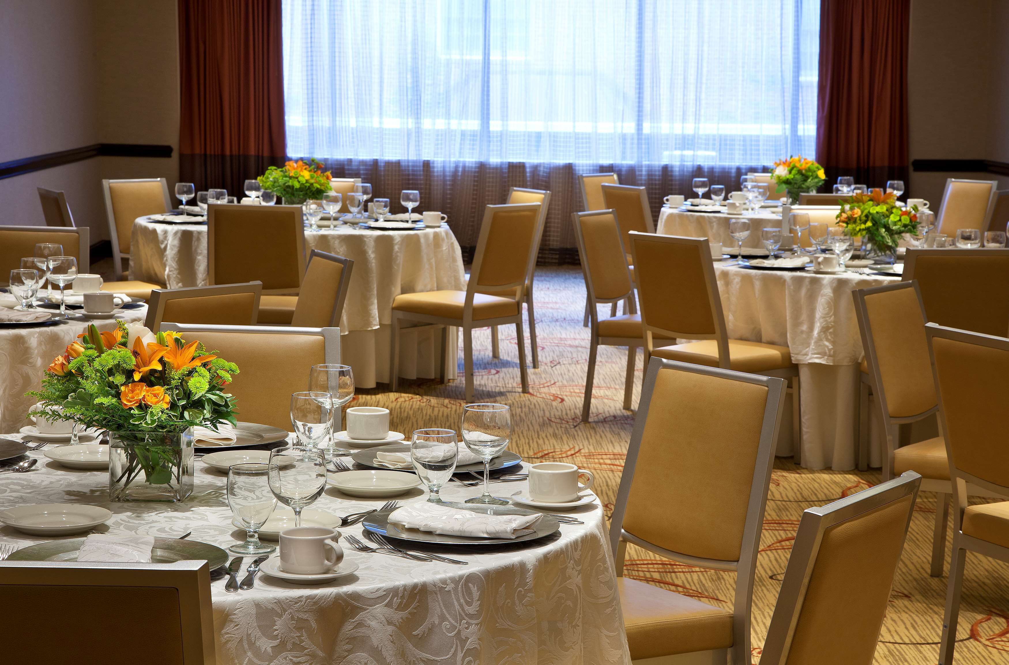 Comedor de hotel con mesas redondas cubiertas con manteles blancos, sillas y centros de mesa florales.