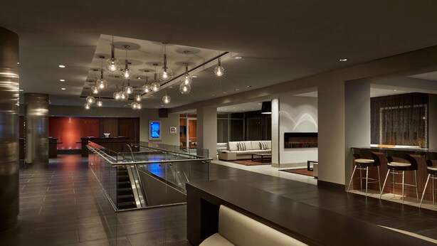 A modern lobby with a central staircase, a bar area with stools, and a seating area with a sofa. - Embassy Suites by Hilton Washington DC Chevy Chase Pavilion (Washington)