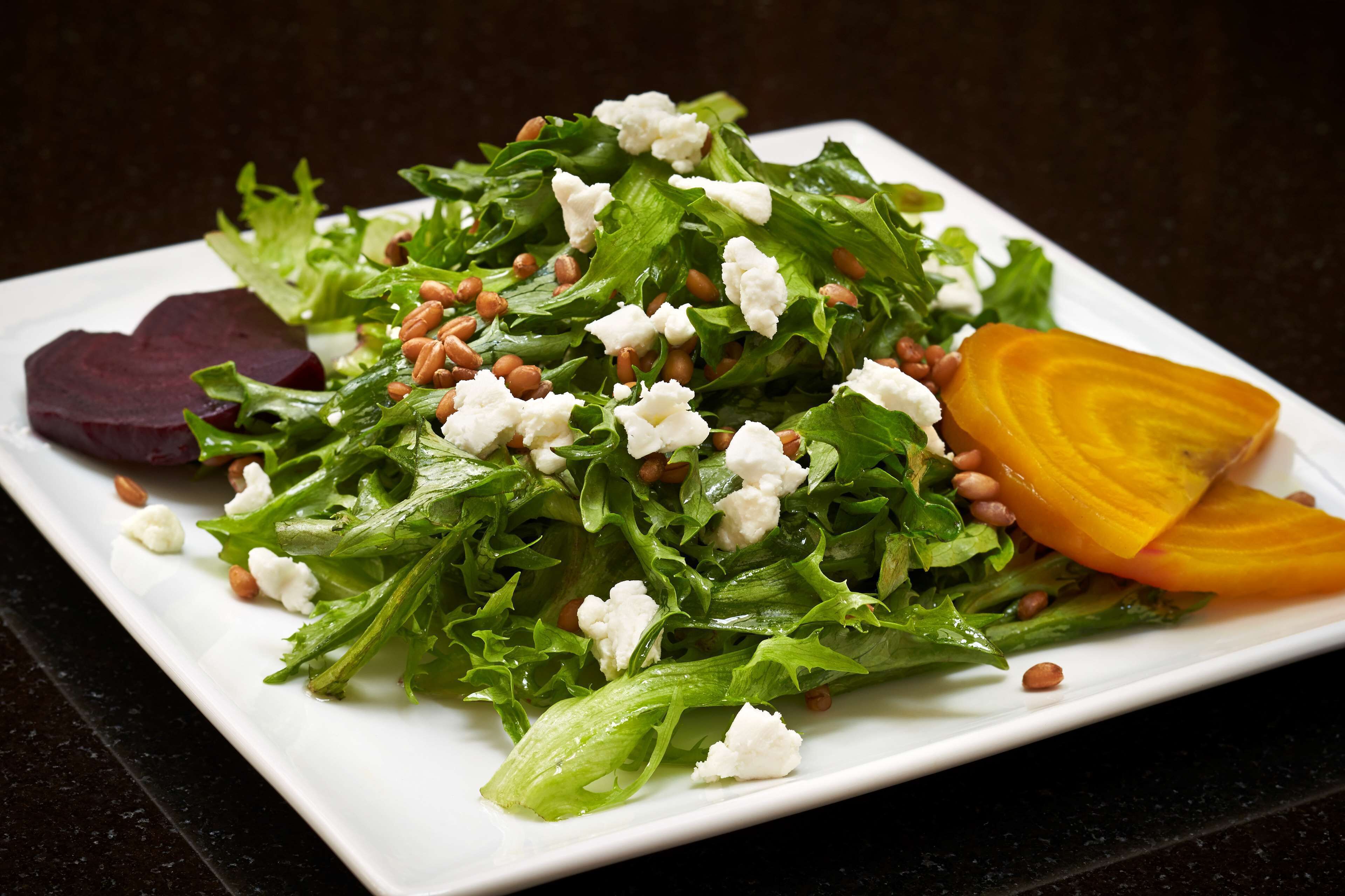 Une salade composée de légumes verts, de fromage feta et de tranches de betteraves, servie dans une assiette blanche.
