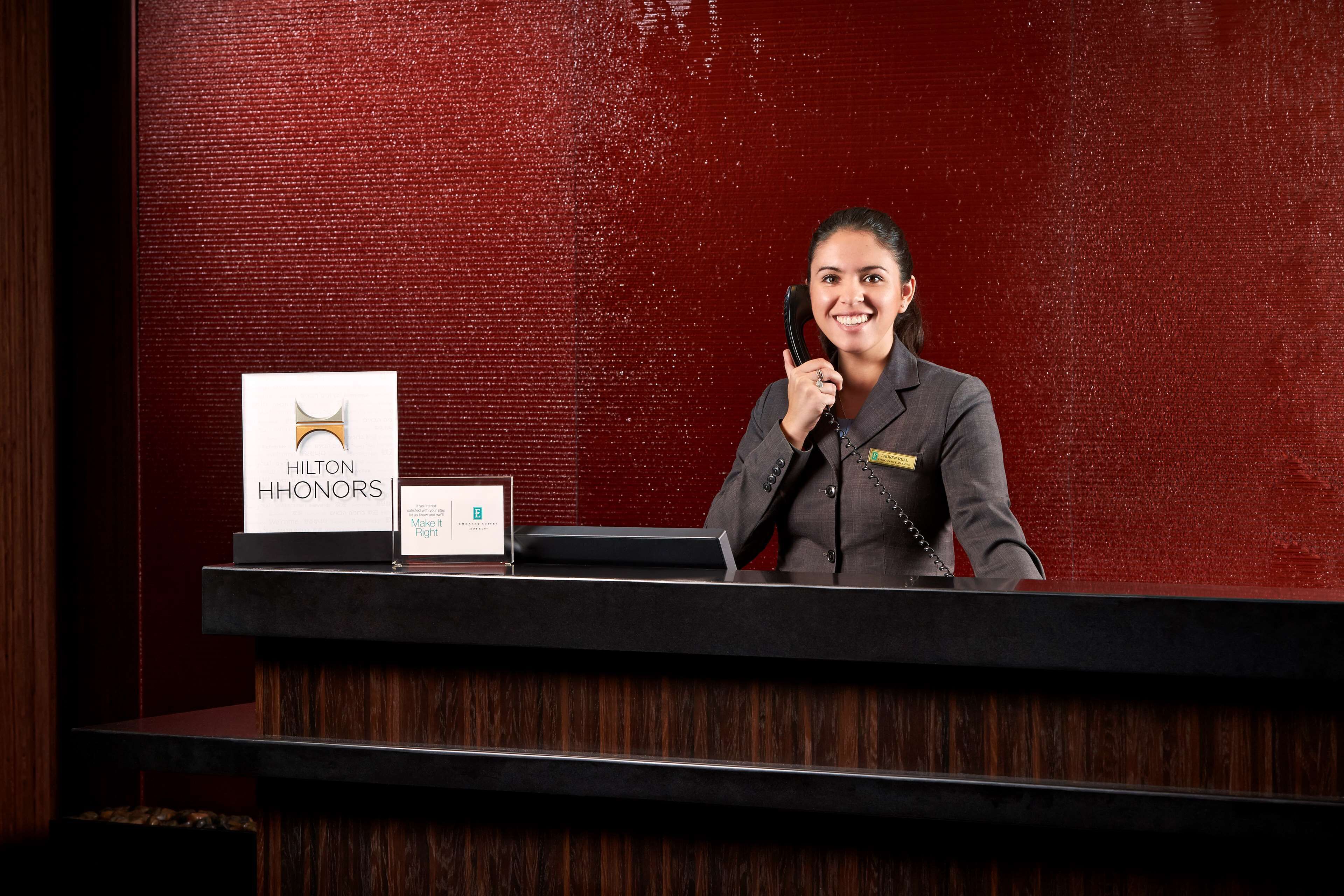 Un mostrador de recepción con una pared texturizada roja, un cartel de Hilton Honors y una placa de identificación.