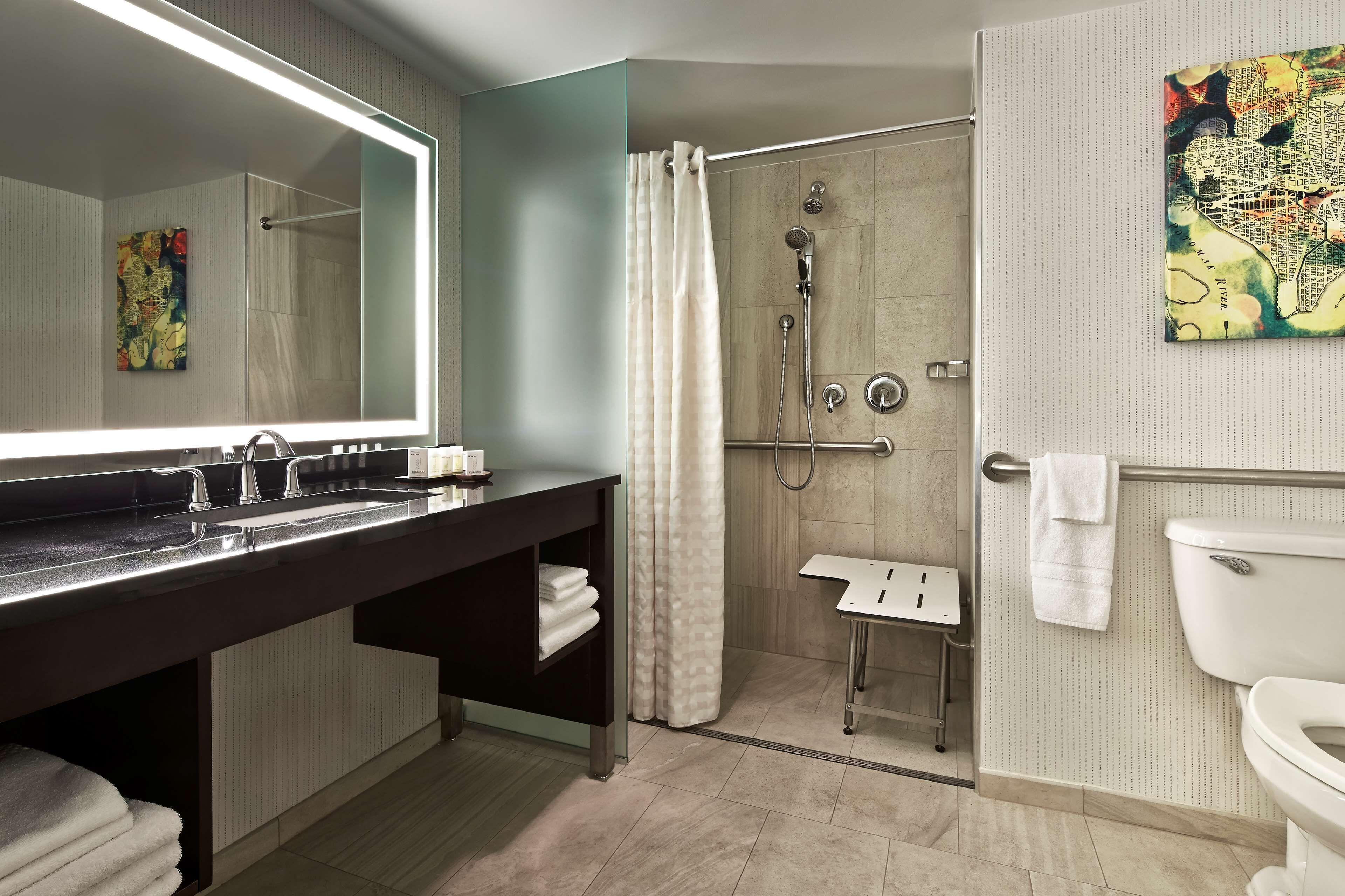 A modern bathroom with a large mirror, a dark vanity, a shower area with a glass door, and a toilet.