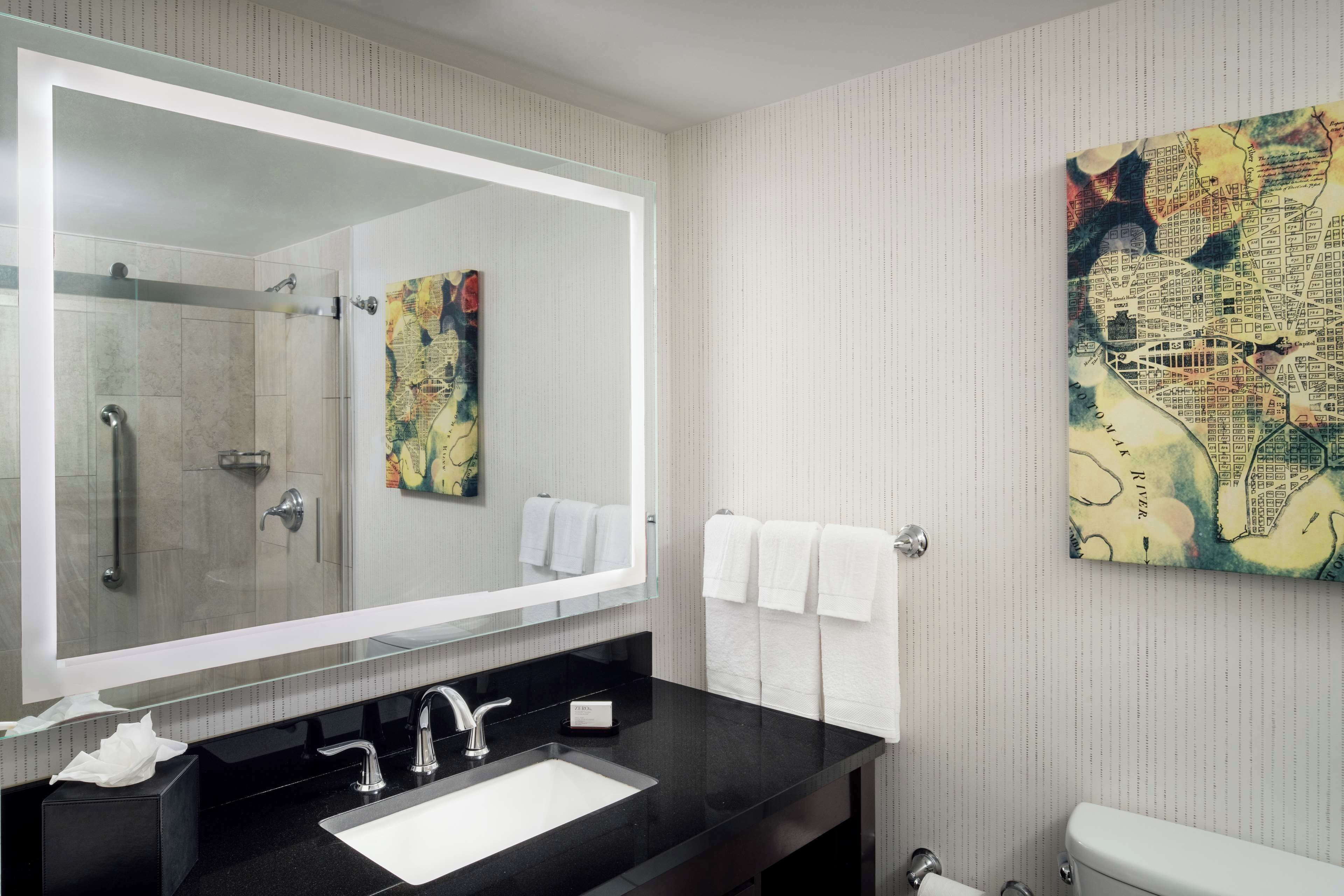 A modern bathroom with a large mirror, black countertop, and a map artwork on the wall.