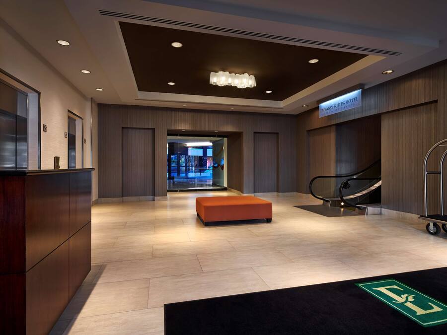 A modern hotel lobby with a reception desk, a seating area, and an escalator.