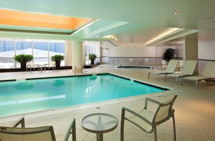 Une piscine intérieure dotée de chaises longues et d’une table, le tout entouré de grandes fenêtres et de plantes en pot.