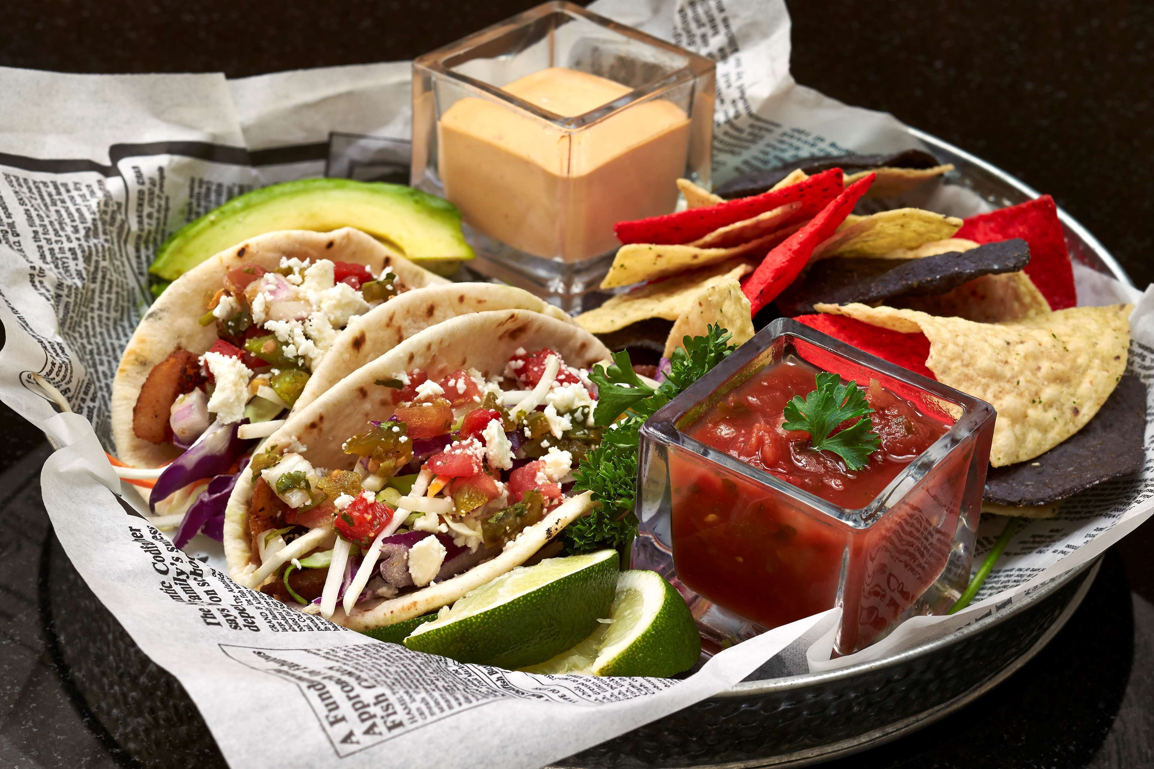 Une assiette avec des tacos, des chips et un petit verre de sauce.