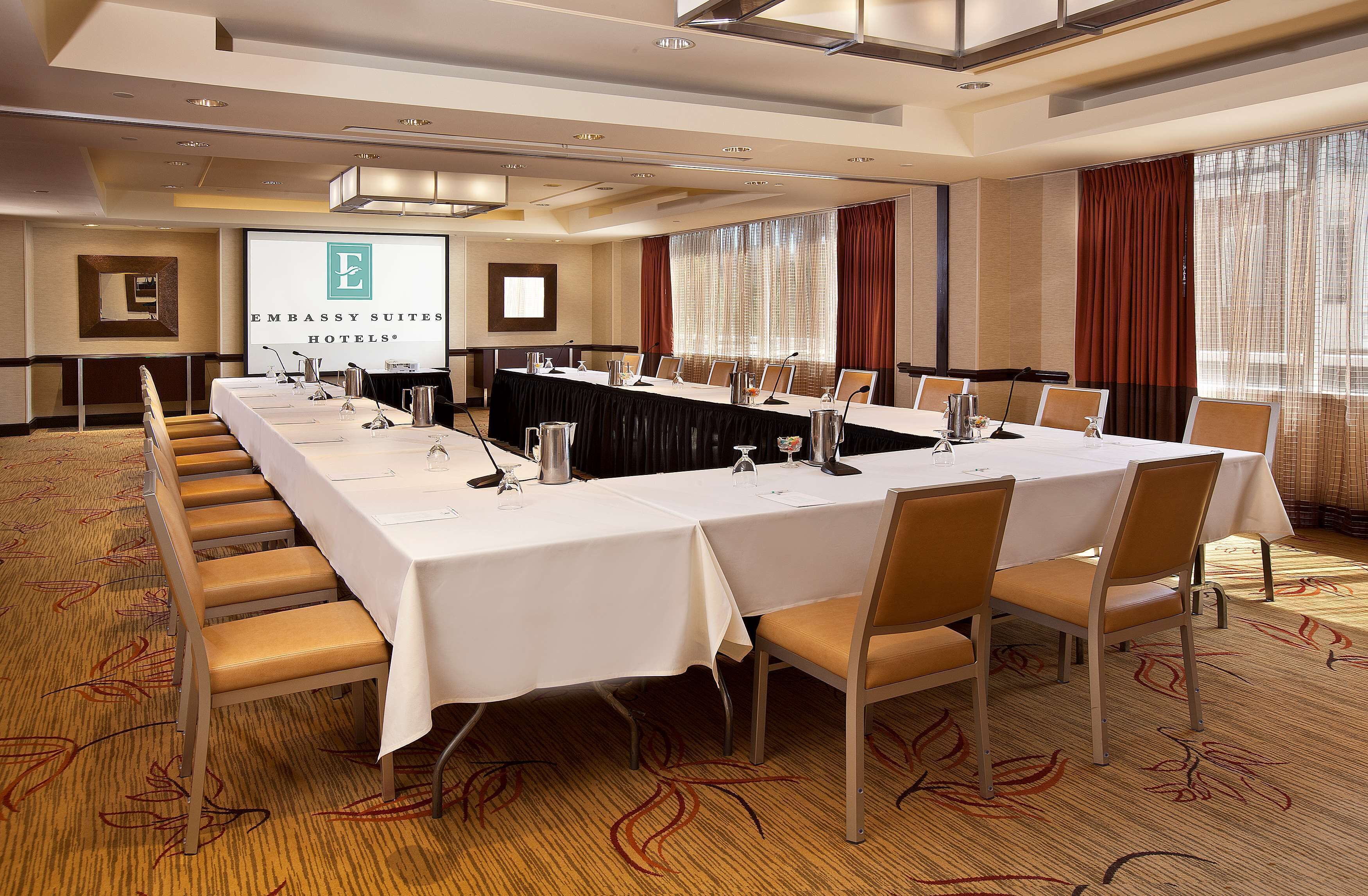 A conference room with a long table, chairs, and a screen displaying the hotel name.