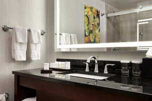 Un baño moderno con un lavamanos negro, un espejo grande y un perchero con toallas blancas.