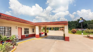 Un Days Inn con fachada roja y color crema, zona de estacionamiento techada y cielo azul despejado con nubes.