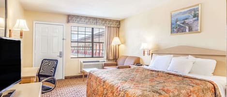 Et hotelværelse med en stor seng, et skrivebord med computer, en stol, et fjernsyn og et vindue med udsigt til bygninger.