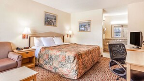 Habitación de hotel con cama, escritorio, silla, televisión y obras de arte en las paredes.