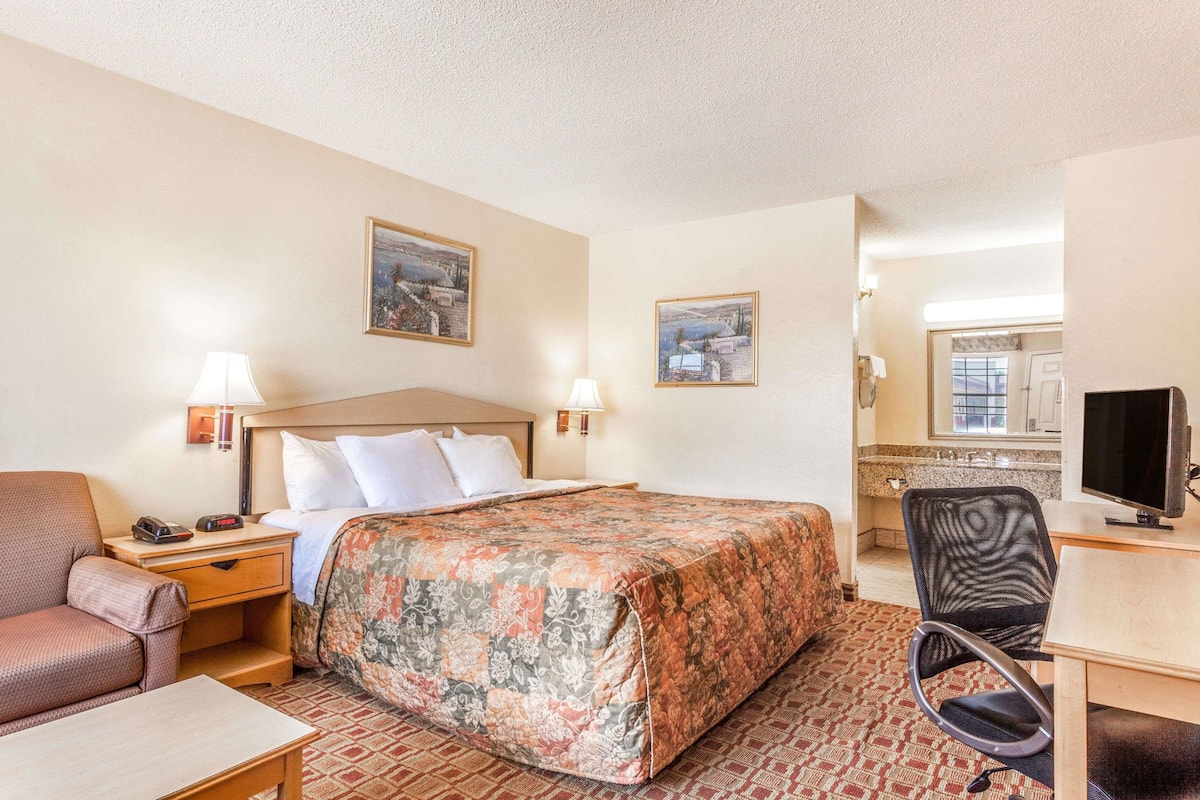 Habitación de hotel con cama, escritorio, silla, televisión y obras de arte en las paredes.
