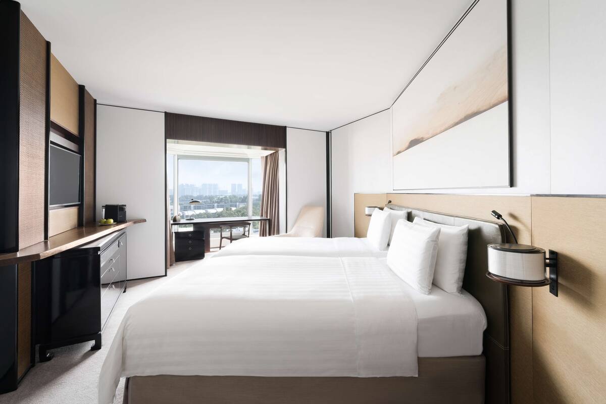 Une chambre d’hôtel avec un grand lit, un bureau, une chaise, une télévision et une fenêtre donnant sur la ville.