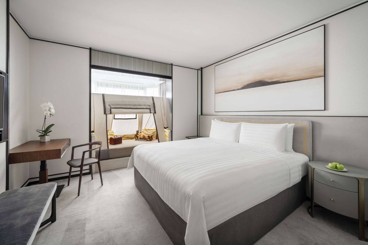 Une chambre d’hôtel moderne, dotée d’un grand lit, d’un bureau, d’une chaise et d’une table de chevet avec une lampe.