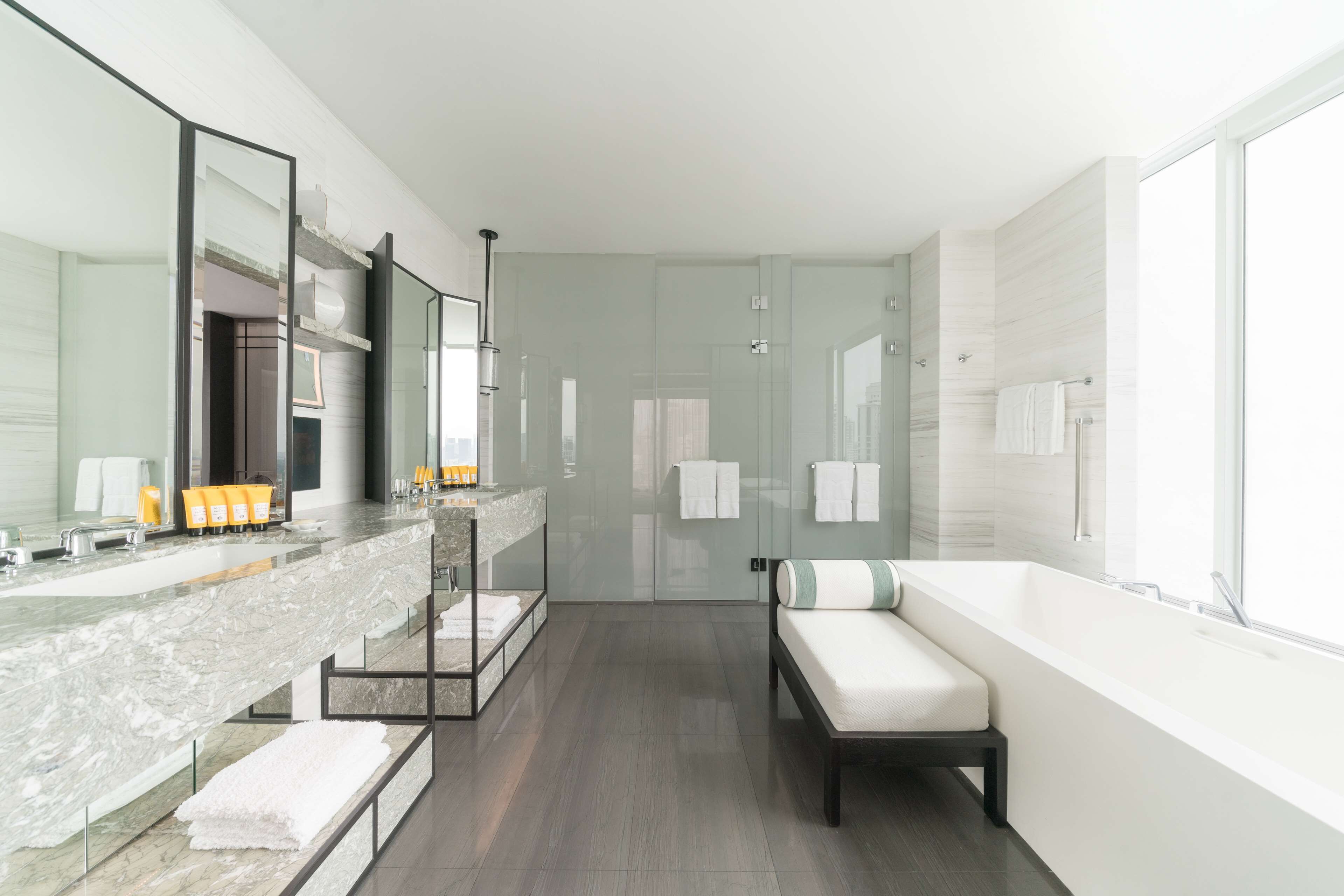 A modern bathroom with a large mirror, a bathtub, and a bench.