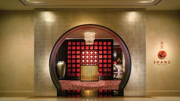 A luxurious lobby with a red and gold color scheme, a chandelier, and a seating area with a patterned rug.