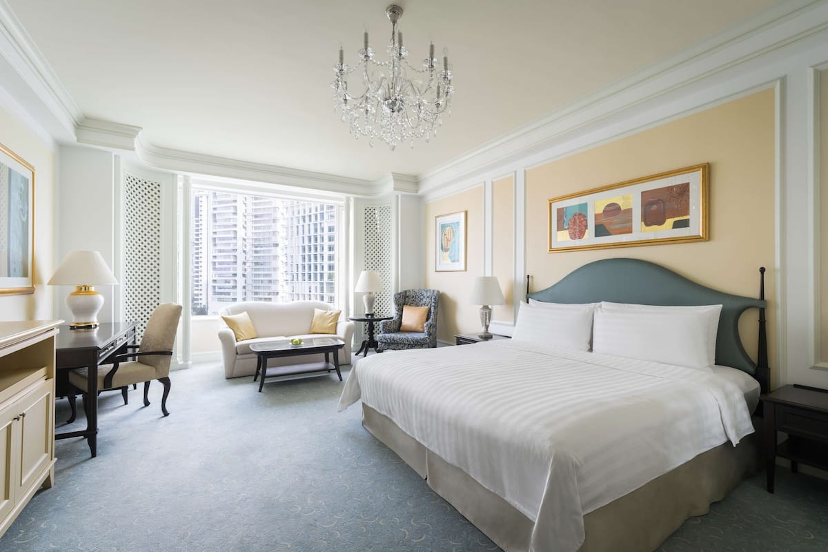 Une chambre d’hôtel spacieuse avec un grand lit, un coin salon comprenant un canapé et des fauteuils, une table à manger et un lustre.