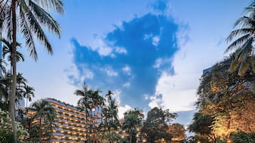 A hotel with a lush garden, palm trees, and a large building with multiple balconies.